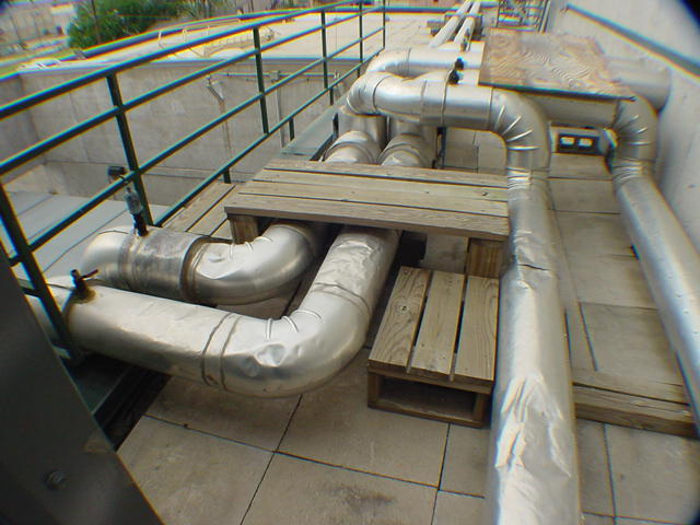 Large insulated chilled water pipes staged on roof skids during 400-ton chiller installation