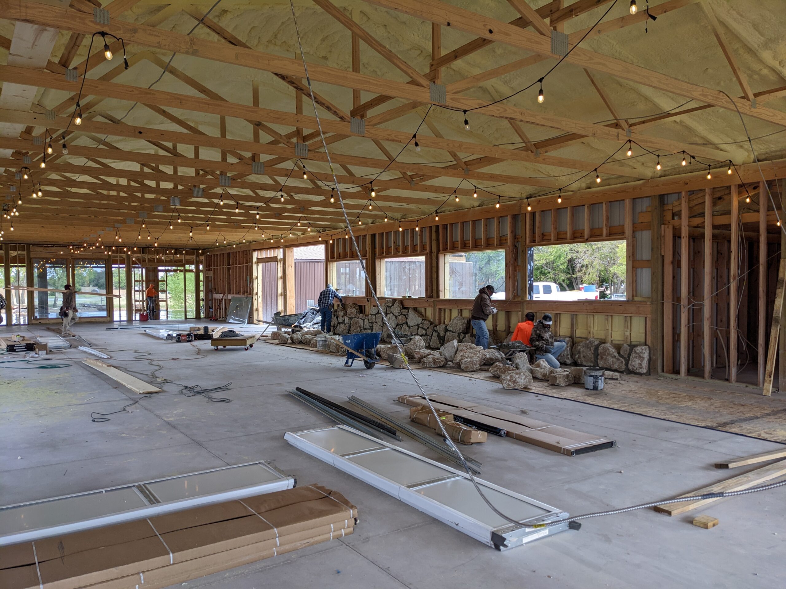 Barndominium event venue under construction with workers building stone wall
