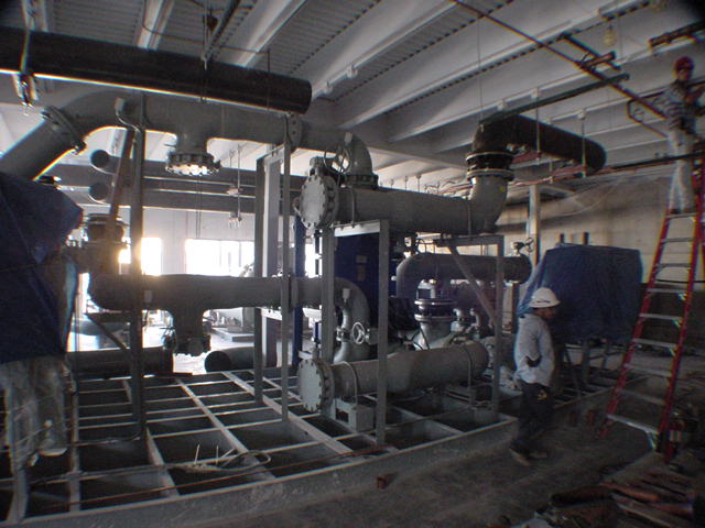 Workers installing large flanged carbon steel chilled water pipes in mechanical room during Sprint project