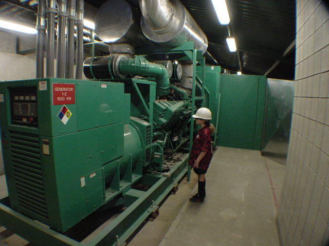 Young technician in hard hat standing next to 1500 KW Cummins generator at commercial data center