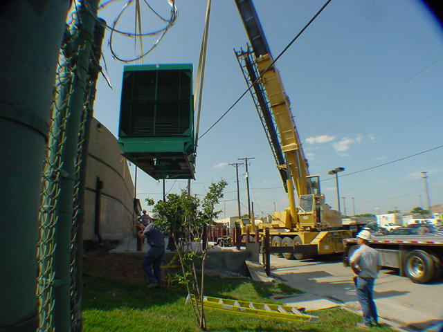 Cummins generator enclosure being crane lifted over razor wire security fence into secured data center