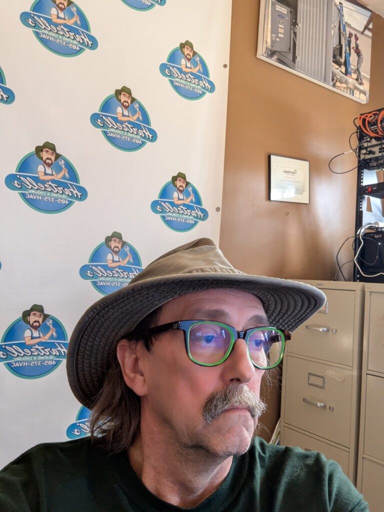 Dave Hartzell, owner of Hartzell's Heat & Air, in office with company logo backdrop — Kingfisher, Oklahoma