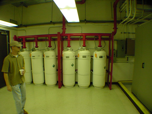 Technician standing next to six Halon 1301 suppression cylinders on red manifold at data center suppression room