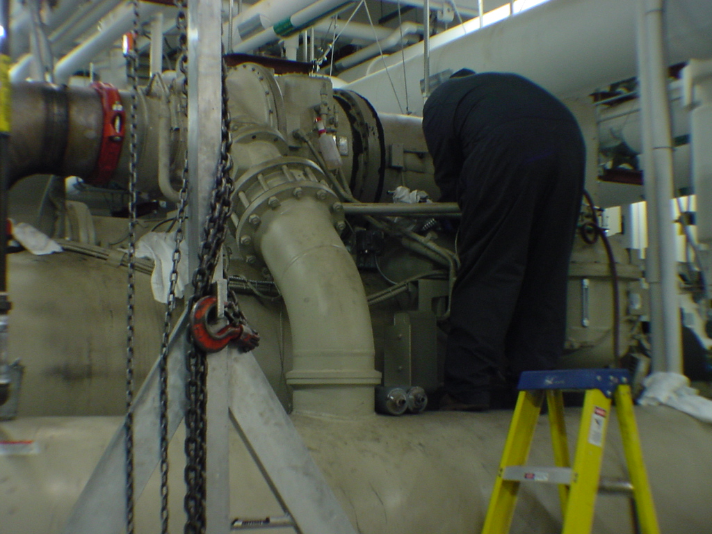 Technician working on McQuay chiller compressor with chain hoist showing scale of machine