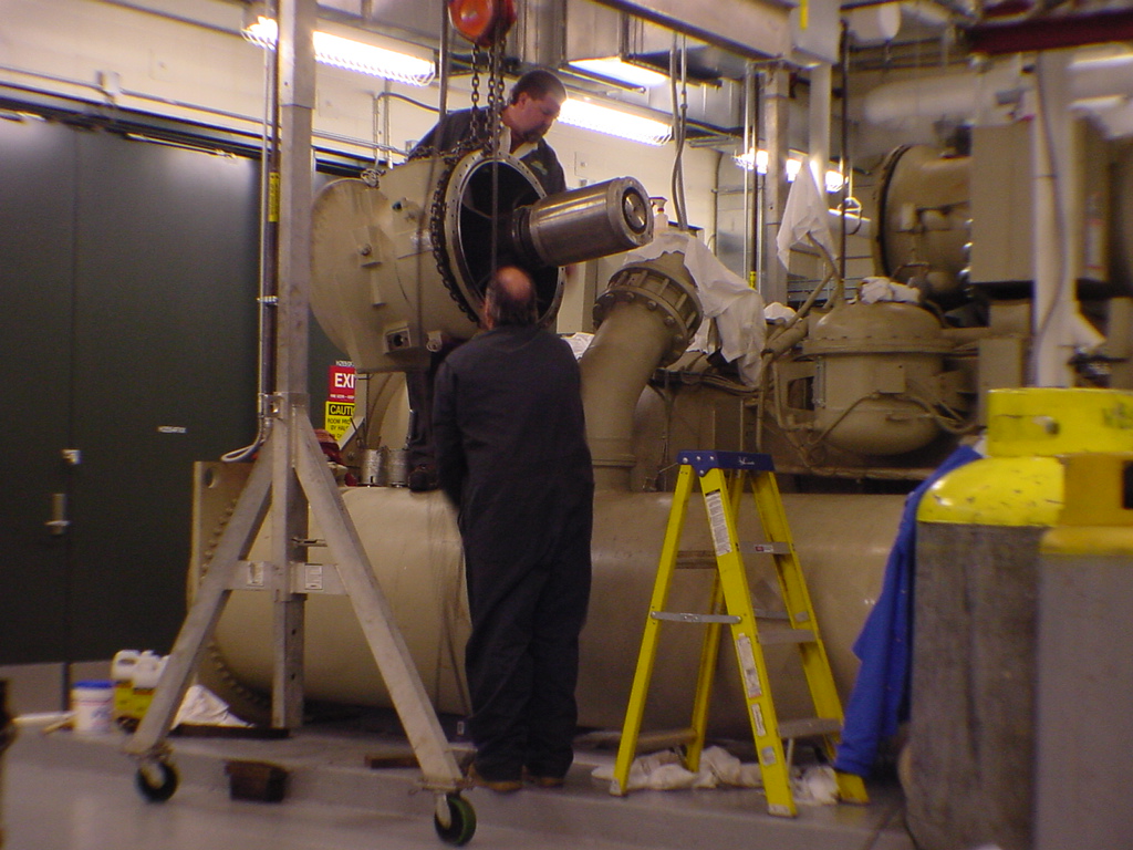 Two technicians reassembling McQuay centrifugal chiller compressor with chain hoist at Sprint data center