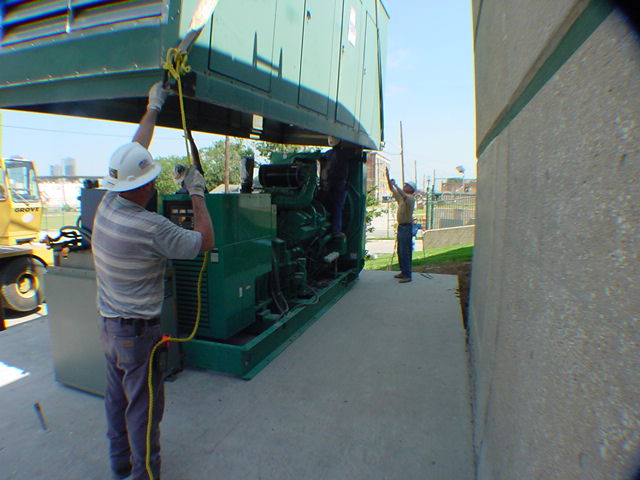 Technician in hard hat guiding Cummins generator enclosure into final position during crane lowering