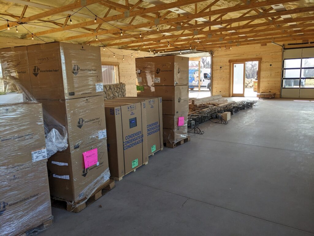 Carrier HVAC equipment staged on pallets inside the open main hall at The Cedar Gate event venue near Loyal, Oklahoma, with exposed wood trusses overhead, during a Hartzell's Heat and Air commercial install