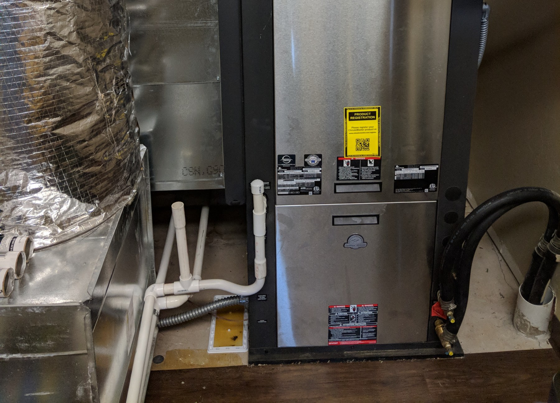 A second ClimateMaster commercial geothermal water-source heat pump with ground-loop hose connections and brass loop valves in a mechanical room at the Wheeler Brothers operation in Watonga, Oklahoma, maintained by Hartzell's Heat and Air