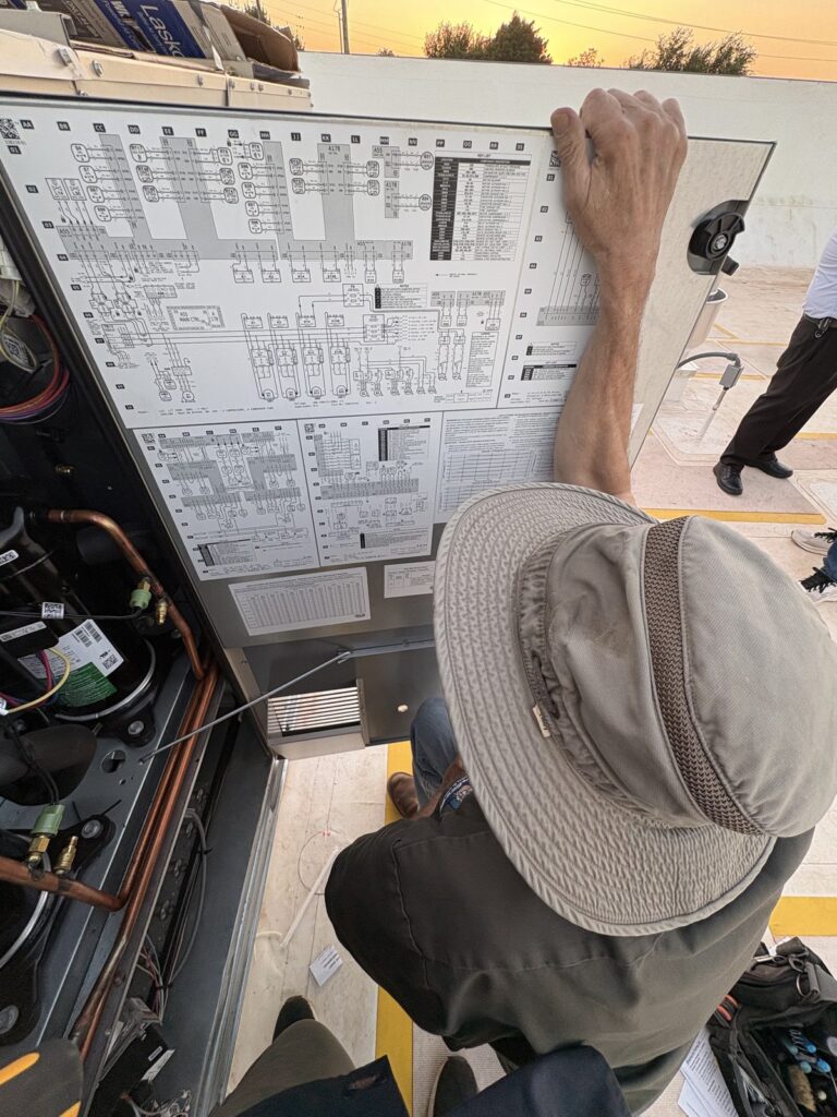 Dave Hartzell in a wide-brim hat reading the wiring schematic mounted inside the open access panel of a commer