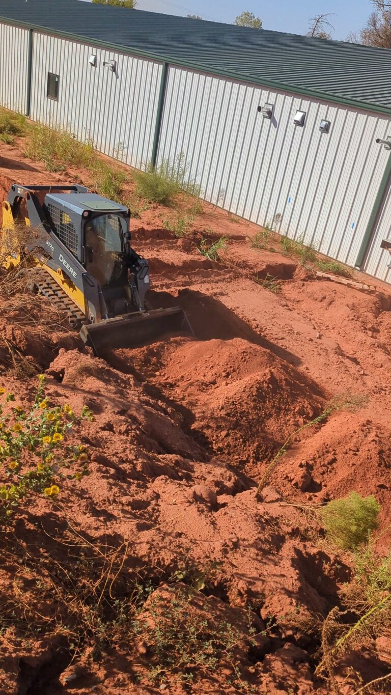 Skid steer moving red dirt at a geothermal trench