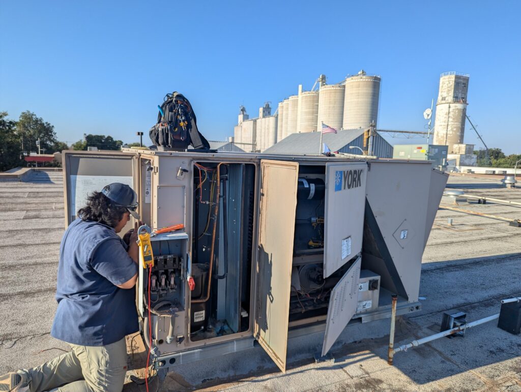 Technician at an open commercial rooftop unit in Watonga Oklahoma with the town grain elevators and water tower visible in the background