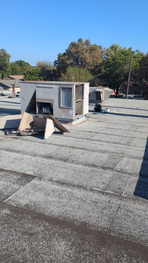 Old commercial rooftop HVAC unit with side panels removed during teardown on a flat roof