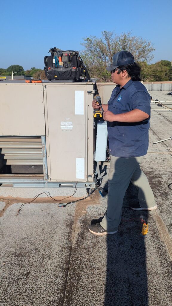 Technician using a drill to wire the electrical disconnect panel on a new commercial rooftop HVAC unit